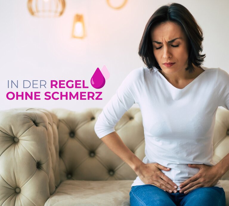 Eine Frau mittleren Alters mit dunklen Haaren sitzt auf einer cremefarbenen Couch und hält sich den Unterbauch, während sie schmerzverzerrt nach unten blickt. Sie trägt ein schlichtes weißes Oberteil und blaue Jeans. Ihr Gesichtsausdruck deutet auf Unbehagen und Bauchschmerzen hin. Über ihr schwebt der Text "IN DER REGEL OHNE SCHMERZ" in Großbuchstaben, begleitet von einem Tropfensymbol. Der Hintergrund ist hell und modern gestaltet, mit dezenten Wandleuchten, die eine warme und einladende Atmosphäre erzeugen. | © GettyImages/Povozniuk [M]