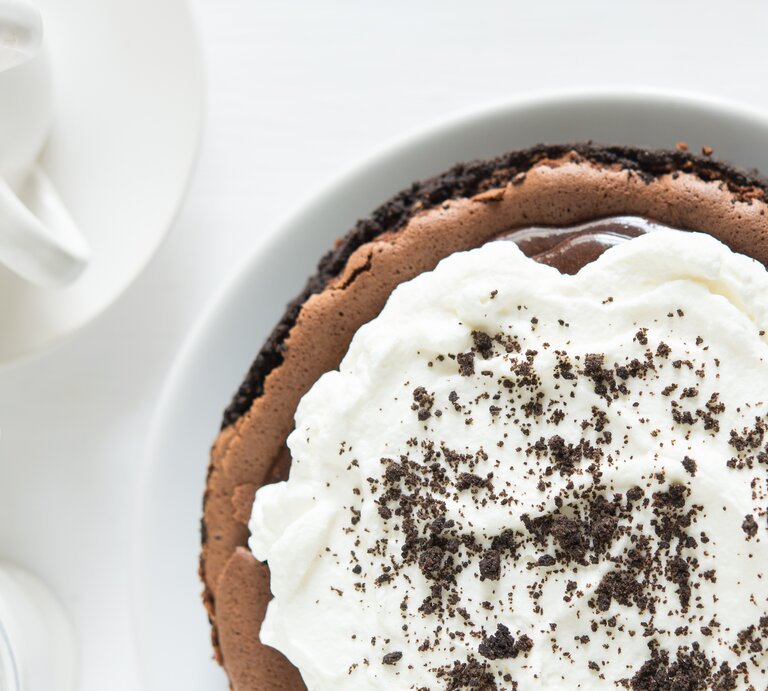 Schokoladenkuchen mit Sahne-Topping auf weißem Untergrund.  | © Shutterstock/pingpongcat