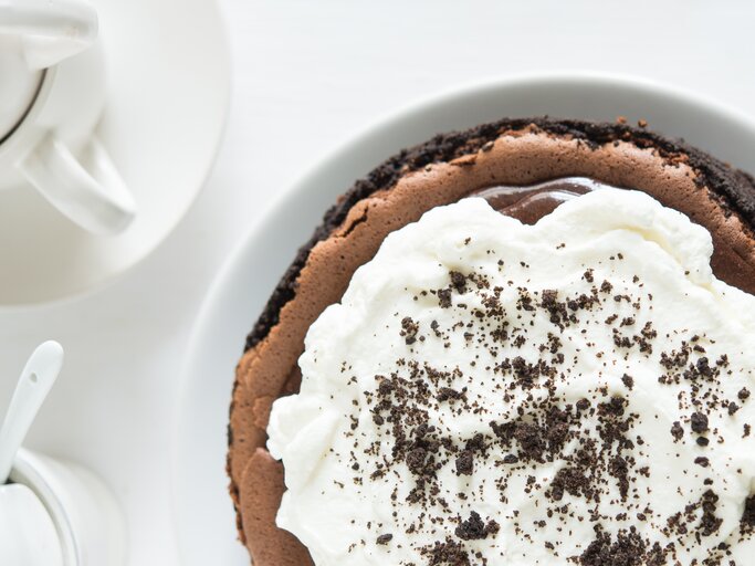 Schokoladenkuchen mit Sahne-Topping auf weißem Untergrund.  | © Shutterstock/pingpongcat