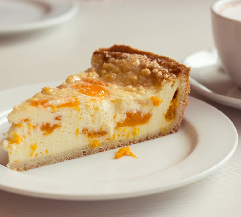 Ein angeschnittenes Stück Mandarinen-Schmandkuchen auf weißem Teller.  | © iStock/ DimaKZ