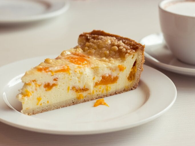 Ein angeschnittenes Stück Mandarinen-Schmandkuchen auf weißem Teller.  | © iStock/ DimaKZ