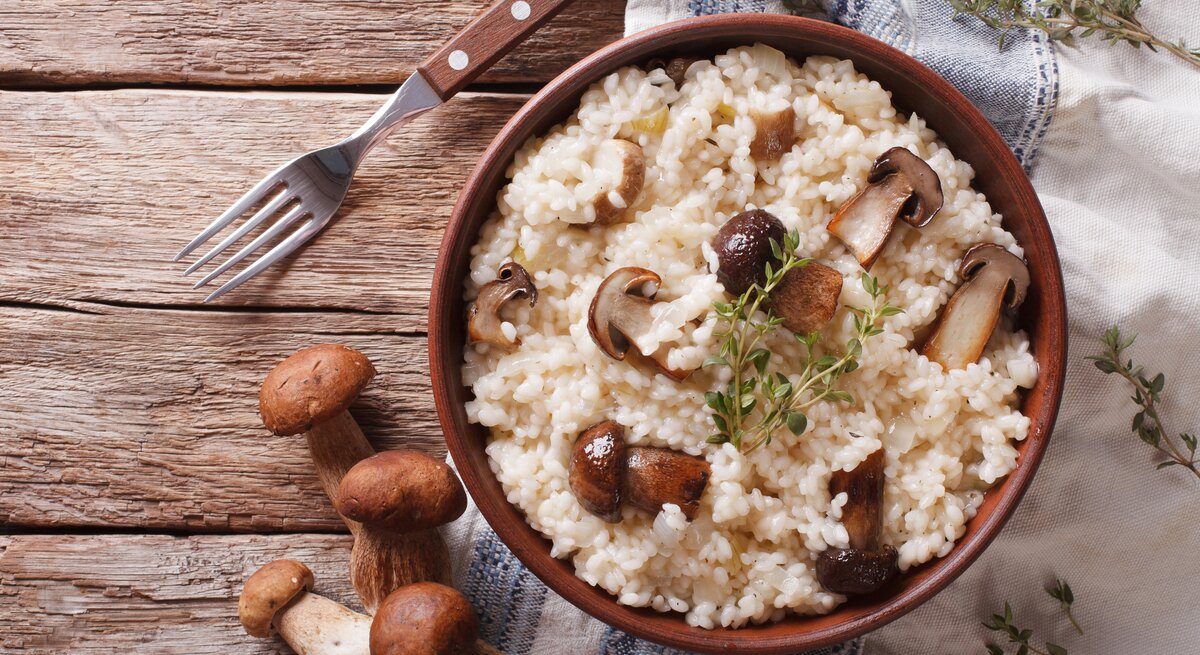 Draufsicht auf einen Teller mit Steinpilz-Risotto auf einem Holztisch.