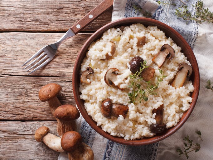 Draufsicht auf einen Teller mit Steinpilz-Risotto auf einem Holztisch. | © iStock/ ALLEKO