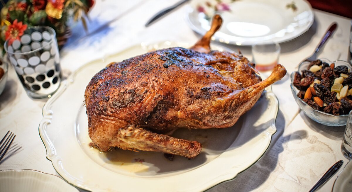 Gänsebraten mit Backpflaumen  auf einem Teller / Drumherum Teller, Besteck und weihnachtliche Dekoration