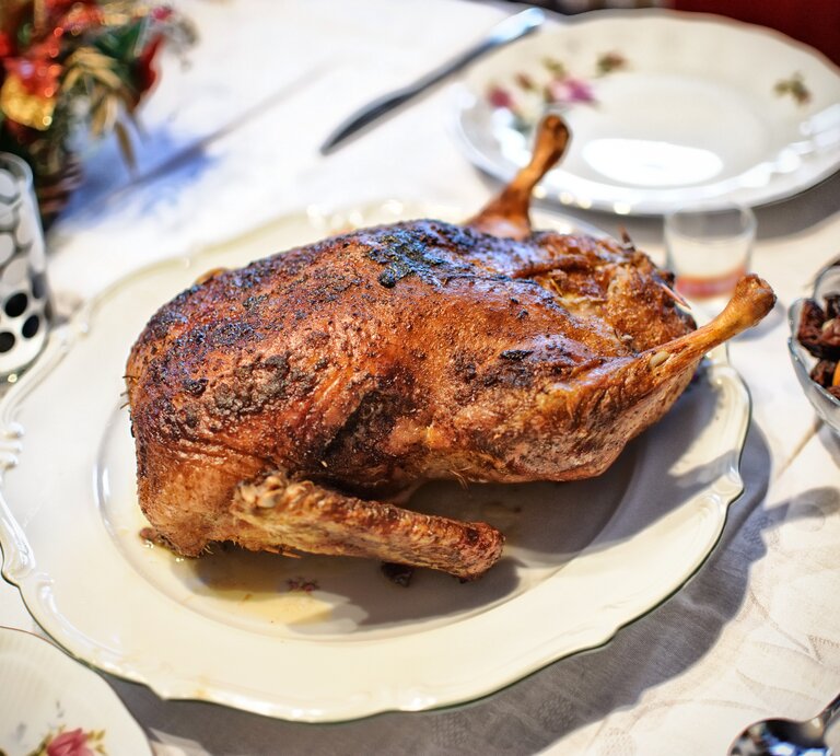 Gänsebraten mit Backpflaumen  auf einem Teller / Drumherum Teller, Besteck und weihnachtliche Dekoration | © iStock/gilotyna