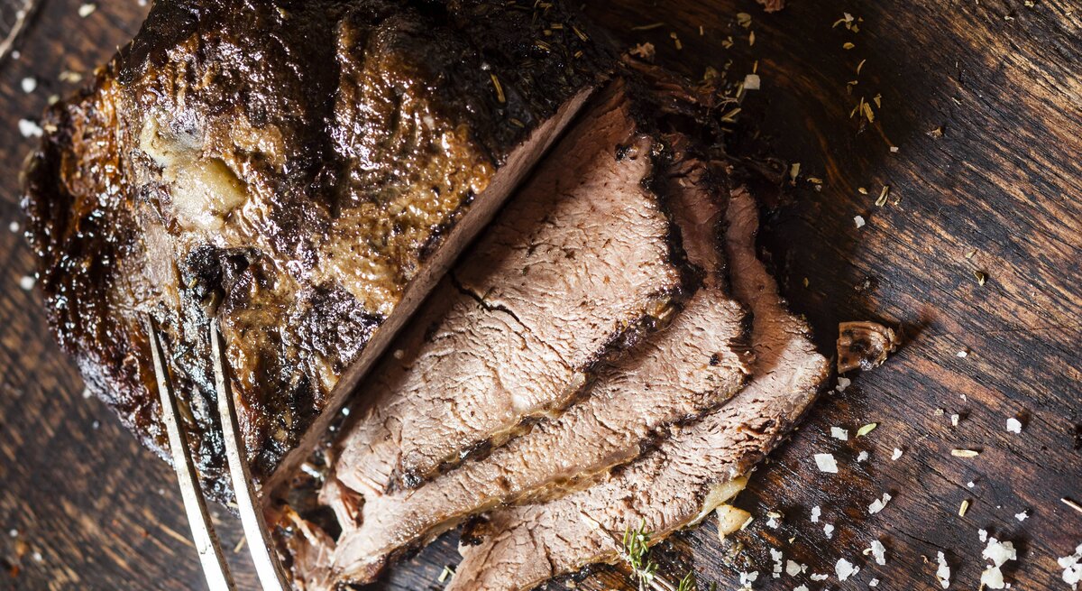 Der angeschnittene Rinderbraten auf einem Holzbrett direkt von oben fotografiert.
