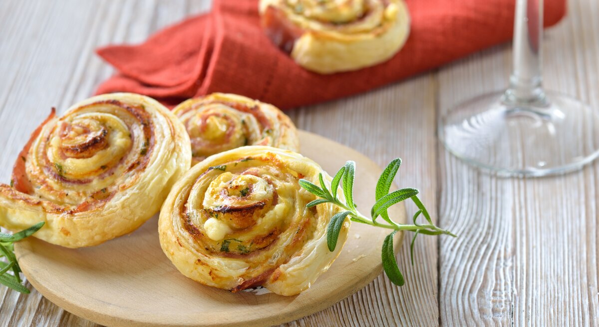 Blätterteigschnecken mit Schinken und Käse  auf hellem Holz. 