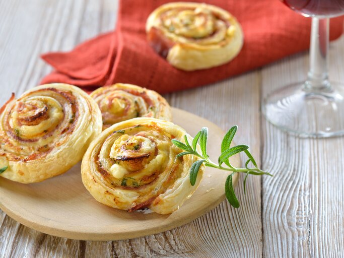 Blätterteigschnecken mit Schinken und Käse  auf hellem Holz.  | © iStock/ kabVisio