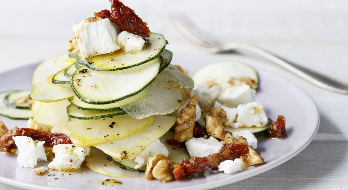 Ein  Teller belegt mit Birnen-Salat mit Zucchini, Ziegenfrischkäse und Walnüssen.