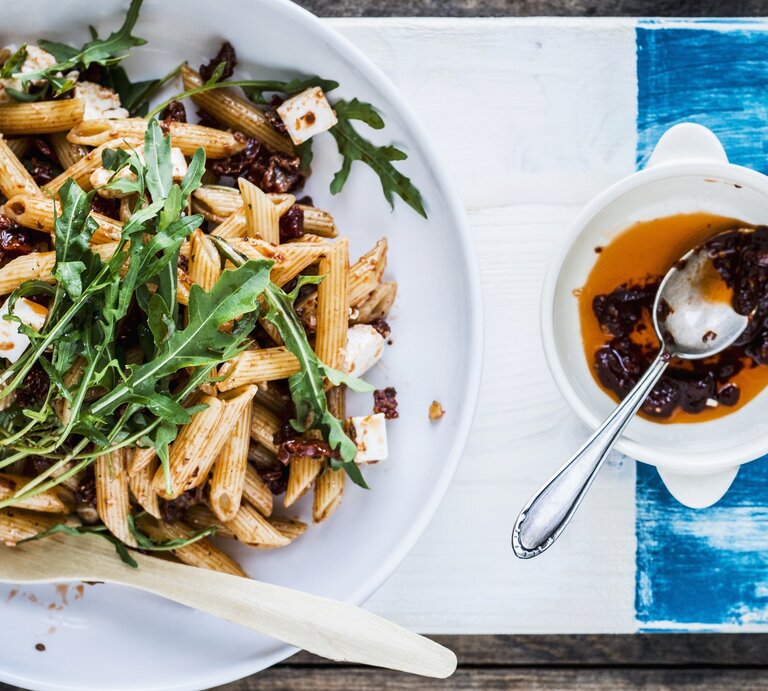 Ein weißer Teller mit dem Nudelsalat auf einem weiß-blauen Tisch direkt von oben fotografiert. | © StockFood