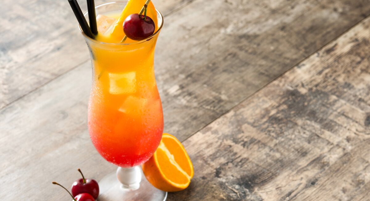 Liebevoll dekoriertes Glas gefüllt mit einem fruchtig aussehendem Cocktail auf Holztisch. 
