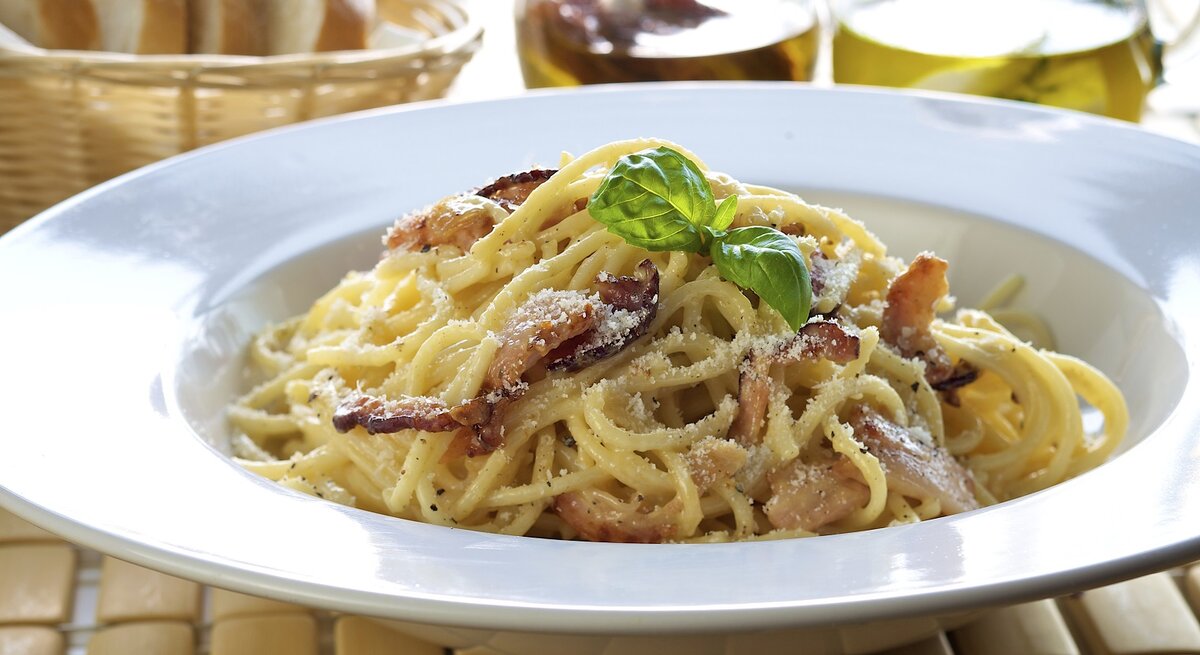 Weißer Pasta-Teller befüllt mit original Spaghetti Carbonara mit italienischem Speck und geriebenem Hartkäse.