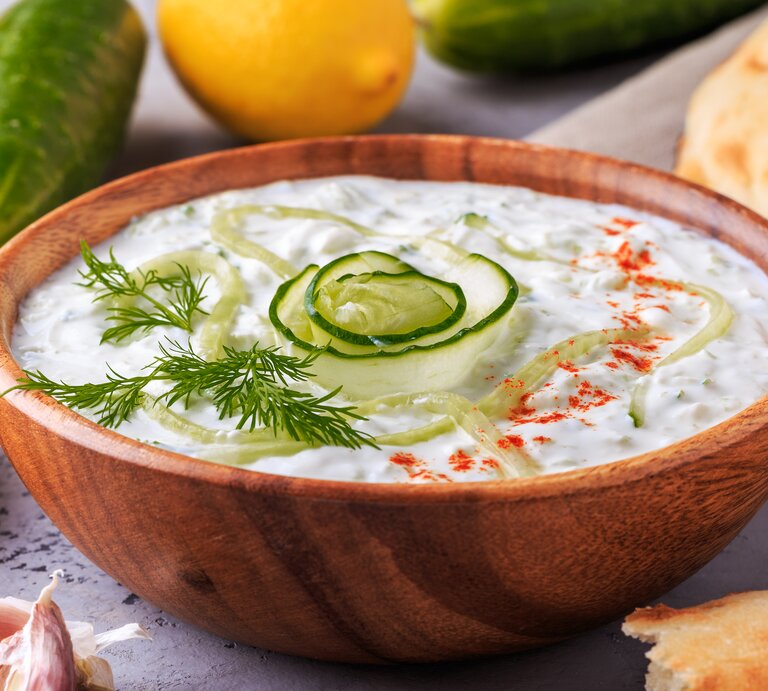 Frischer Zaziki mit Gurke in einer Holzschale. Daneben liegen Gurken, Knoblauch, Zitronen und Brot.  | © iStock/ tbralnina 