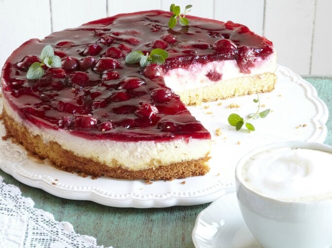 Die angeschnittene Kirsch-Schmand-Torte seitlich auf einem weißen Kuchenteller und hellem Tisch. | © Matthias Liebich