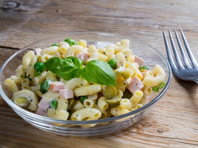 Durchsichtige Schale gefüllt mit Nudelsalat mit Fleischwurst und Erbsen.  | © iStock/ 8vFanI 