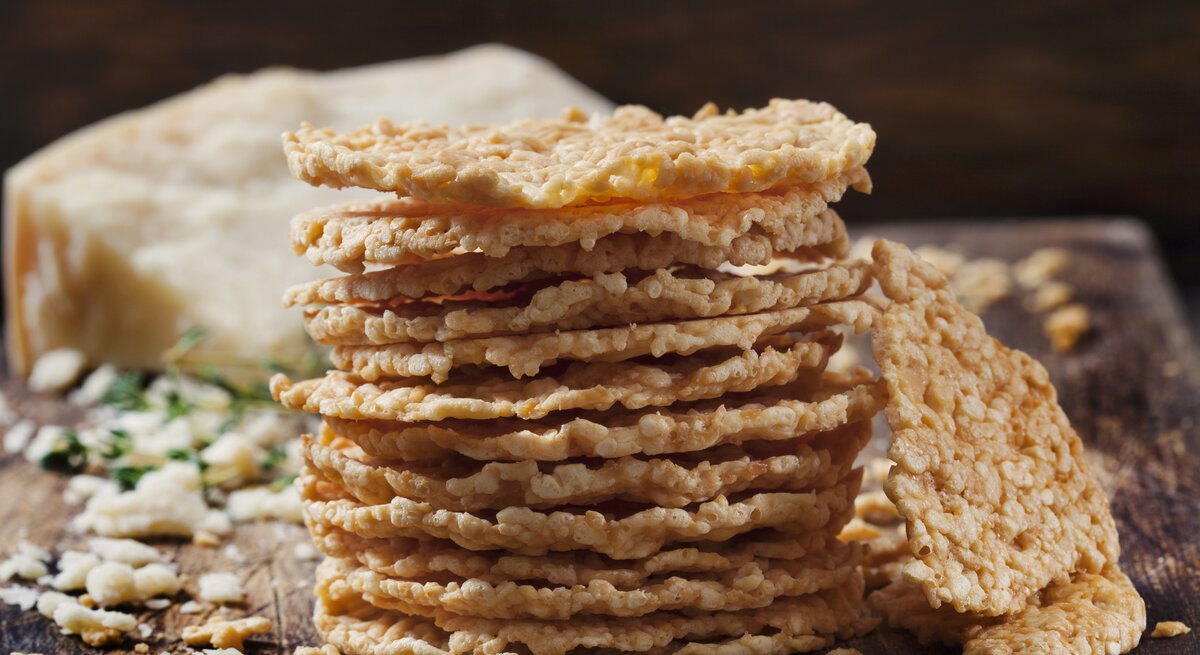 Stapel gebackene Käse-Cracker auf Holzbrett vor dunklem Hintergrund. 