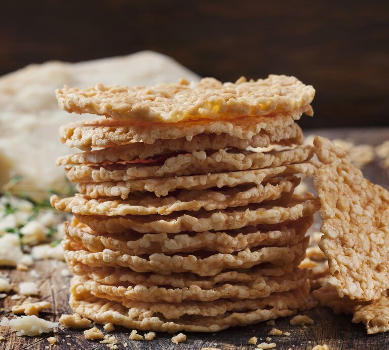 Stapel gebackene Käse-Cracker auf Holzbrett vor dunklem Hintergrund.  | © iStock.com/LauriPatterson
