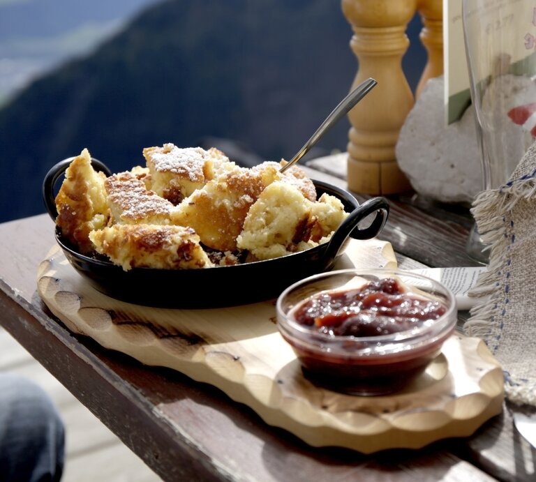 Bananenschmarrn in Pfanne auf Holzbrett, daneben Kompott Schälchen | © GettyImages/Westend61