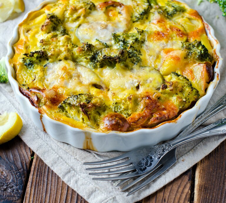 Eine weiße Auflaufform mit dem Gratin auf einem rustikalen Holztisch mit weißer Tischdecke. | © iStock/ Teleginatania