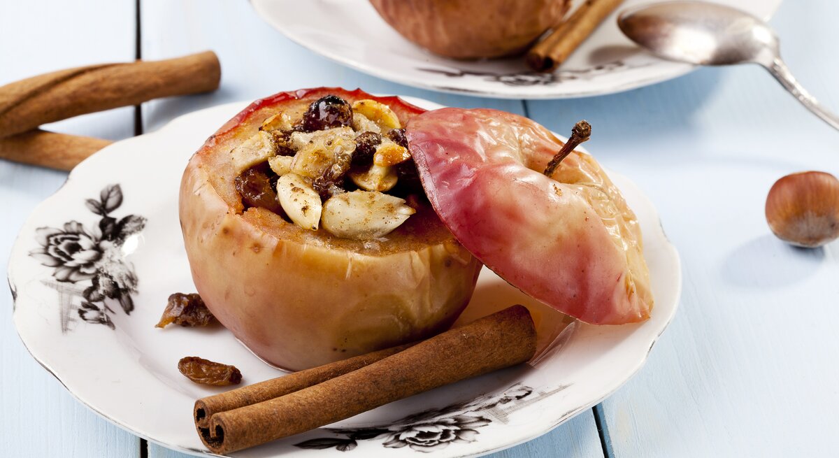 Ein gefüllter Bratapfel mit Knusperhaube auf weißem Teller. 