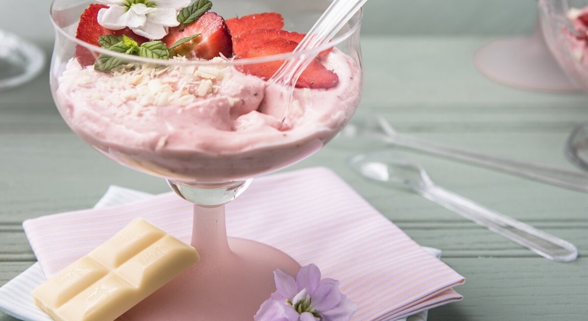 Draufsicht, eint schräg von oben: Eine weiße Schokoladenmousse mit Mascarpone und Erdbeeren in einem Glas.