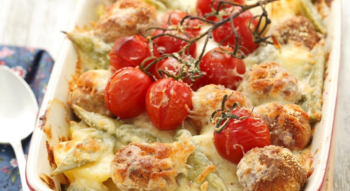 Kartoffelauflauf mit Hackbällchen und Tomaten in weißer Auflaufform. 