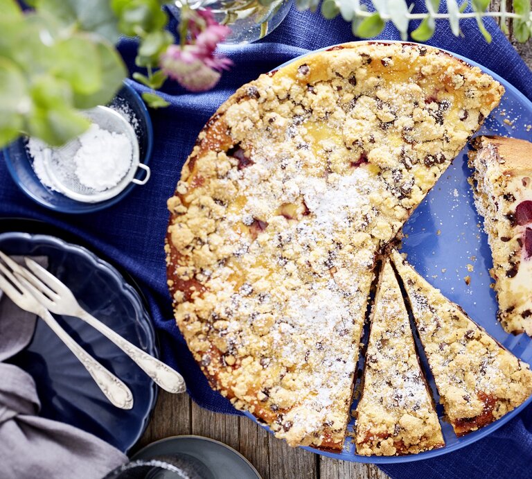 Der Käse-Kirsch-Streuselkuchen auf einem Holztisch mit blauer Tischdecke. Alles direkt von oben fotografiert. | © Eat Club/Isabell Triemer