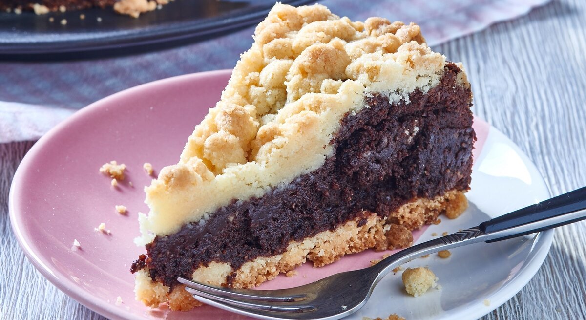 Ein angeschnittenes Stück Schokoladenkuchen mit hellem Streusel-Topping auf einem Teller.
