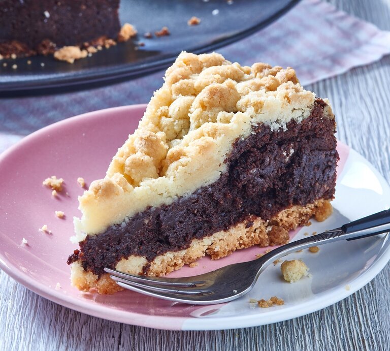 Ein angeschnittenes Stück Schokoladenkuchen mit hellem Streusel-Topping auf einem Teller.