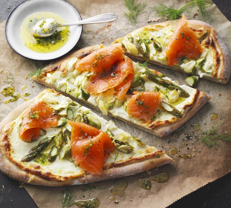 Flammkuchen mit grünem Spargel und Räucherlachs auf Backpapier und dunklem Tisch. | © StockFood / Gräfe & Unzer Verlag / Kramp + Gölling