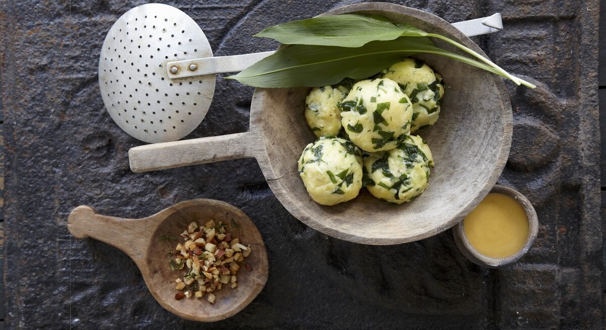 Die Bärlauch-Kartoffelknödel in einer weißen Marmorschale mit der Sauce Bernaise auf einem dunkelgrauem Untergrund.