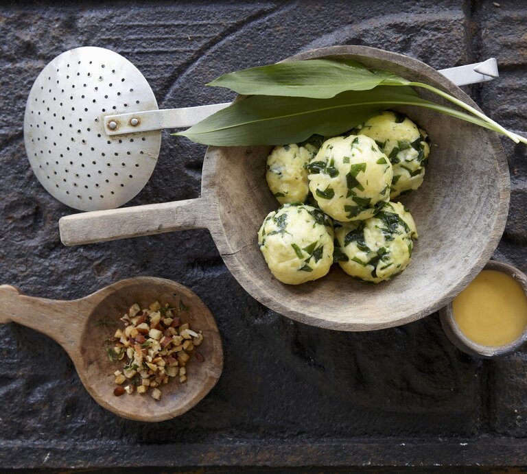 Die Bärlauch-Kartoffelknödel in einer weißen Marmorschale mit der Sauce Bernaise auf einem dunkelgrauem Untergrund. | © StockFood / Schütz, Anke