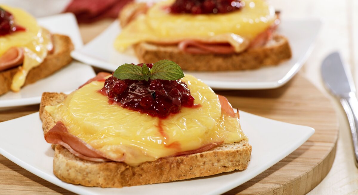 Das Toast Hawaii auf einem weißen Teller und Holzuntergrund. Alles von der Seite fotografiert.