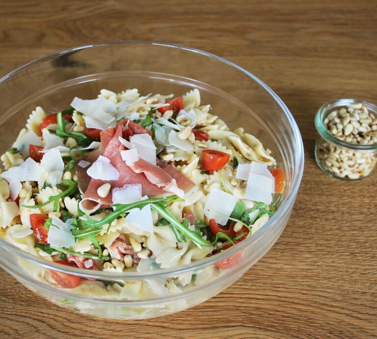 Eine Glasschüssel mit dem Nudelsalat auf einem hellen Holztisch. Alles von schräg oben fotografiert. | © BILD der FRAU-Redaktion