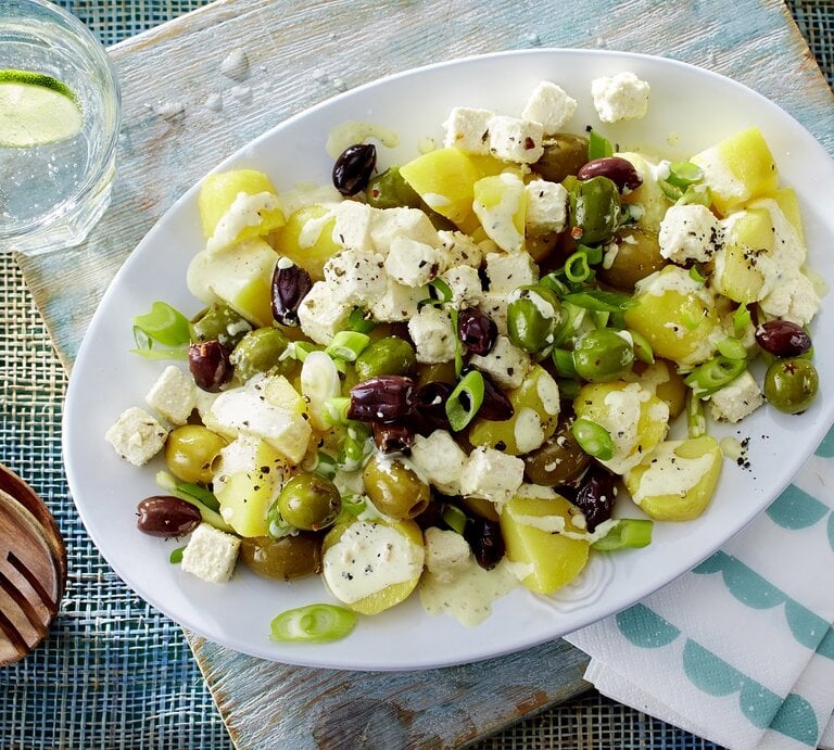 Griechischer Kartoffelsalat mit Hirtenkäse und Oliven / ovaler Teller / Salatbesteck aus Holz / Draufsicht / Nahaufnahme | © Redaktionsagentur Food & Foto / Bauer Food Experts KG