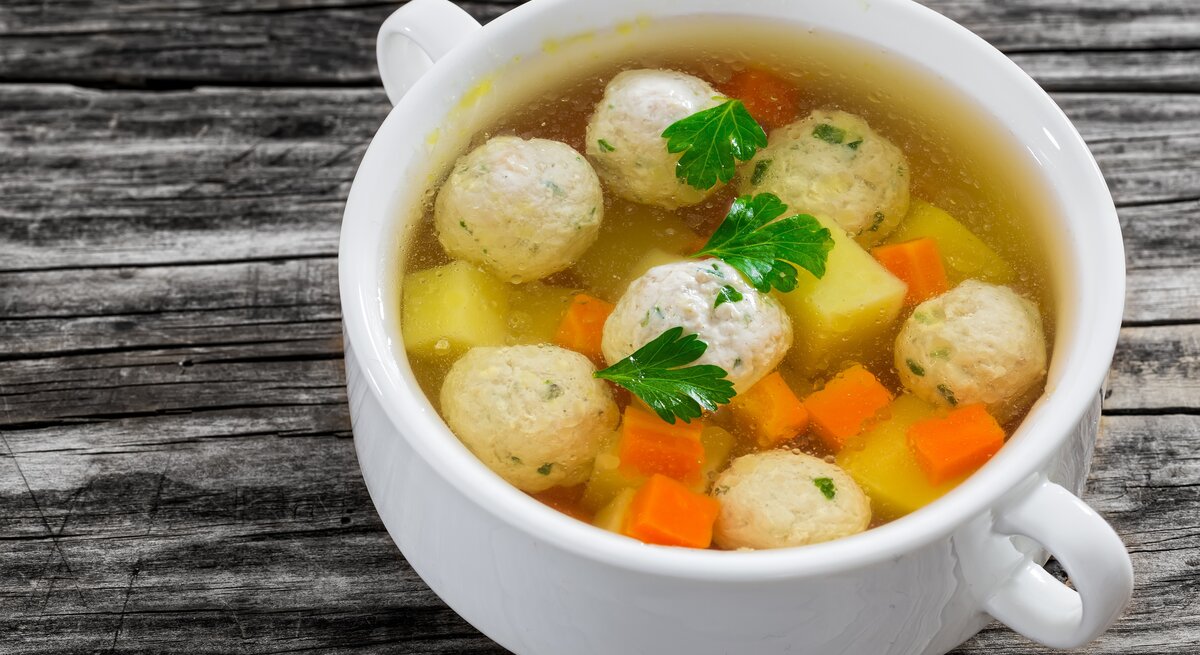Weiße Suppenschüssel gefüllt mit Hochzeitssuppe mit Bällchen auf einem dunklen Holztisch. 