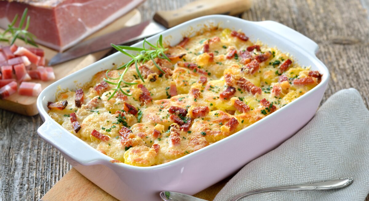 Eine weiße Auflaufform mit dem Gratin auf einem Holztisch von schräg oben fotografiert.