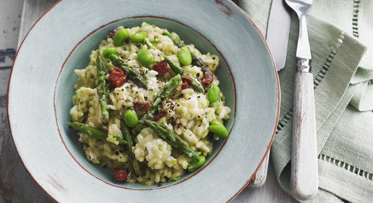 Ein hellblauer Teller mit dem grünen Risotto auf einem grauen Holztisch mit hellen Tischdecken. Alles direkt von oben fotografiert.
