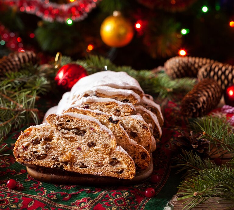 Ein angeschnittener Stollen umringt von vielen weihnachtlichen Deko-Elementen.  | © iStock/ GreenArtPhotography