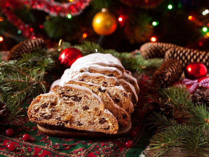 Ein angeschnittener Stollen umringt von vielen weihnachtlichen Deko-Elementen.  | © iStock/ GreenArtPhotography