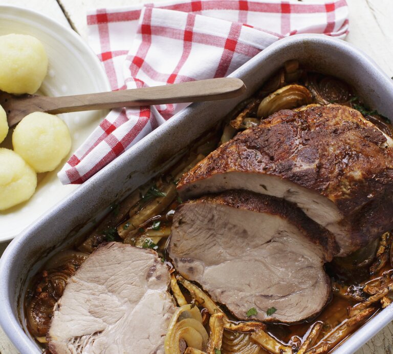 Bräter mit Schweinebraten in Soße, daneben ein Teller voll Knödel.  | © StockFood / Gräfe & Unzer Verlag / Bonisolli, Barbara