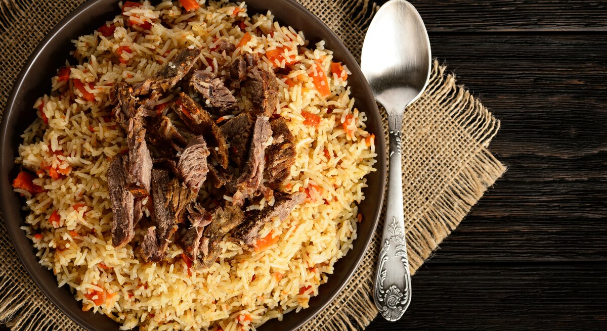 Draufsicht auf eine Reispfanne mit gebratenem Rindfleisch auf braunem Teller. 