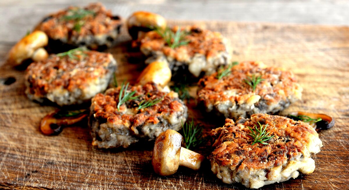 Mehrere vegetarische Pilzfrikadellen auf einem Holzbrett. 