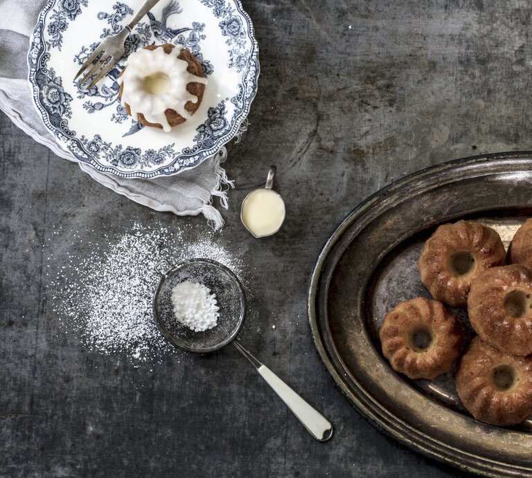 Die kleinen Kuchen auf einem dunklen Tisch mit blauweißem Teller. Alles direkt von oben fotografiert. | © StockFood / Dee's Küche