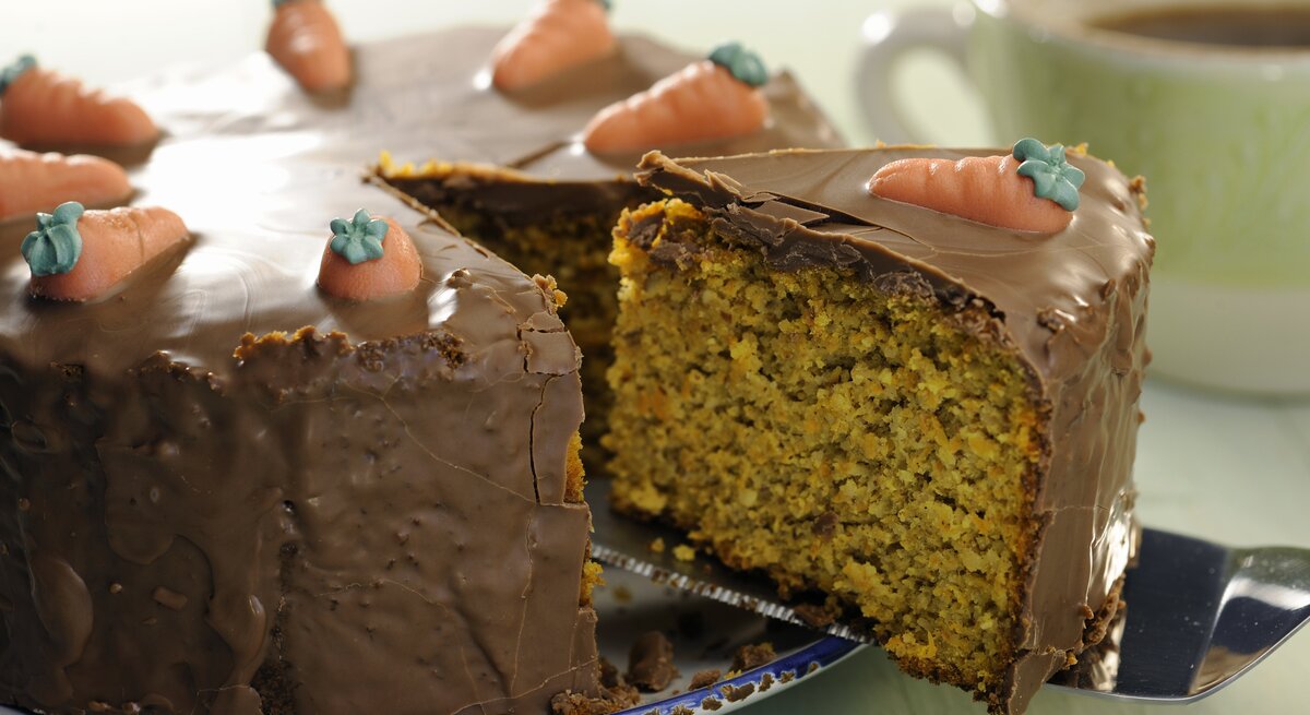 Eine Nahaufnahmen vom Schoko-Möhrenkuchen und gerade wird ein angeschnittenes Stück rausgenommen mit dem Tortenheber.