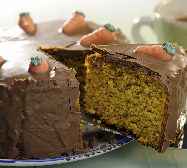 Eine Nahaufnahmen vom Schoko-Möhrenkuchen und gerade wird ein angeschnittenes Stück rausgenommen mit dem Tortenheber. | © iStock/Silberkorn