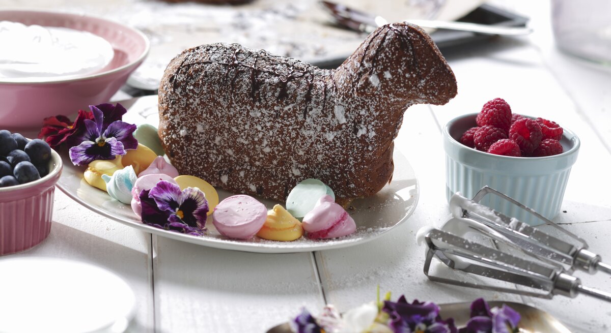 Auf einem hellen Holztisch liegt ein gebackenes Osterlamm mit Baisertupfen.