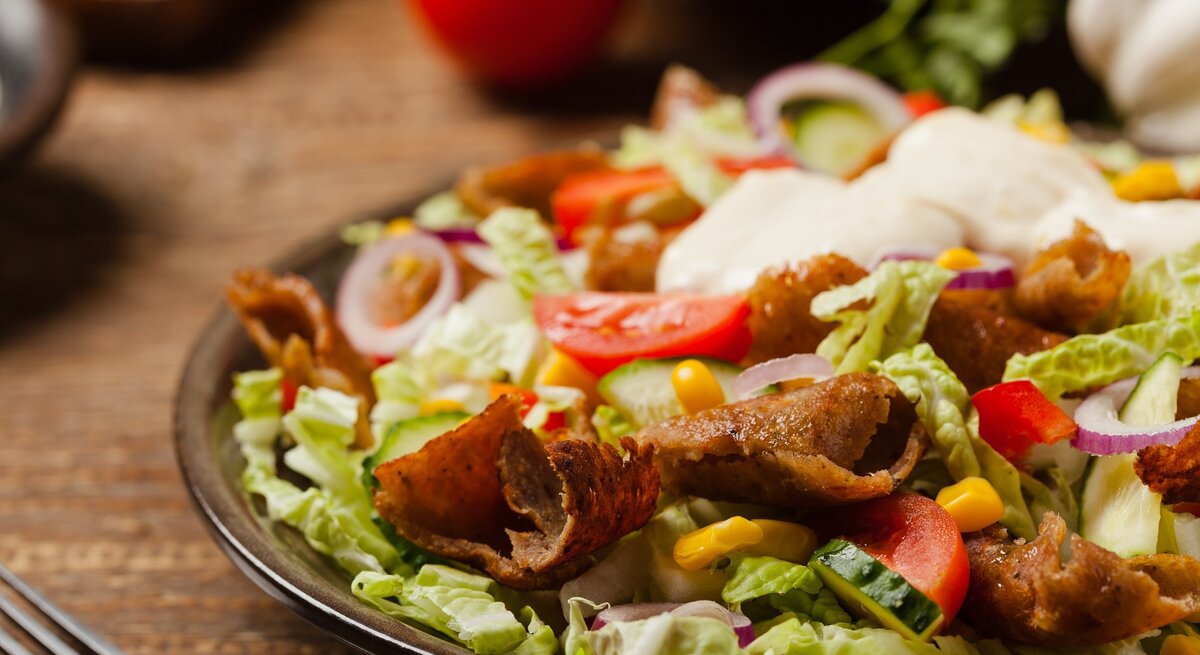 Ein schwarzer Teller auf einem Holztisch mit dem Gyros-Salat von der Seite fotografiert.