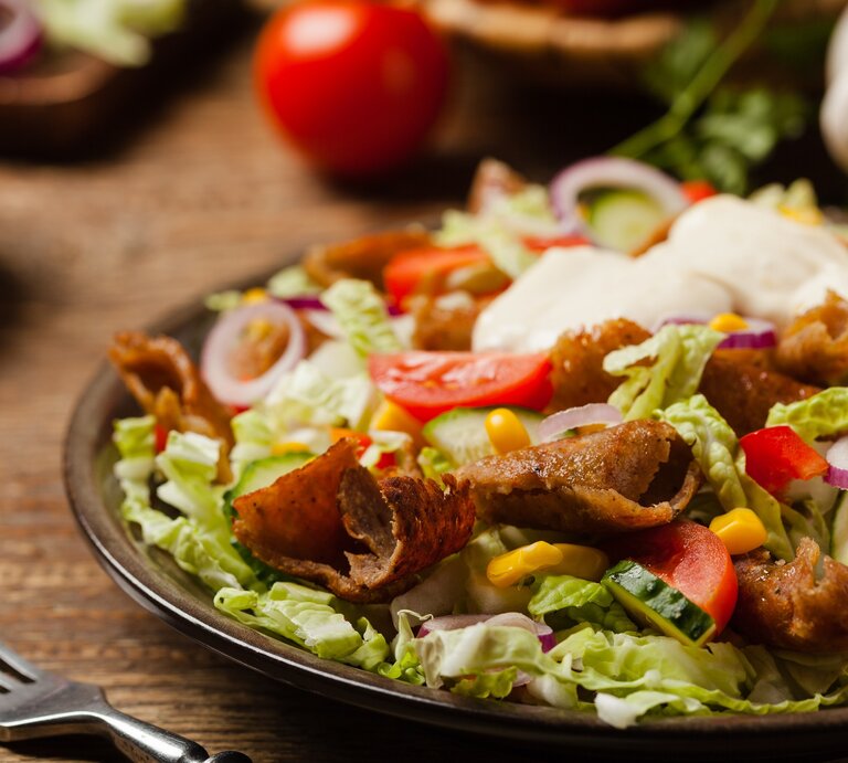 Ein schwarzer Teller auf einem Holztisch mit dem Gyros-Salat von der Seite fotografiert. | © Shutterstock/ gkrphoto