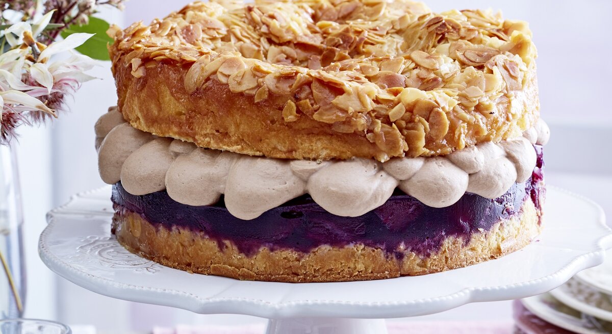 Frontal fotografierter Bienenstich mit Nougatsahne und Rotwein-Birnenkompott auf einer Etagere.